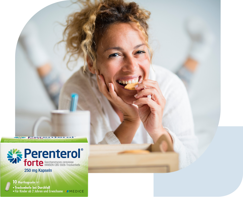 Eine Perenterol forte Verpackung, mit einer lächelnden Frau, die in einen Keks beißt im Hintergrund