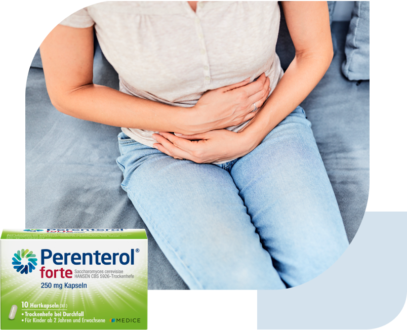 Eine Perenterol forte Verpackung, mit einer Frau mit Magenbeschwerden, die auf einem Sofa sitzt im Hintergrund