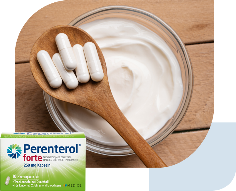 Tabletten liegen auf einem Holzlöffel, der auf einer Schüssel mit Joghurt liegt. Perenterol Packung liegt über dem Bild.