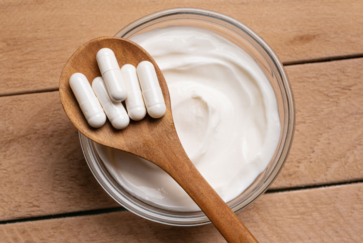 Tabletten liegen auf einem Holzlöffel, der auf einer Schüssel mit Joghurt liegt.