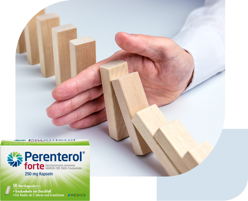 Eine Perenterol forte Verpackung, mit ein paar umfallenden Dominosteinen, die von einer Hand gestoppt werden im Hintergrund