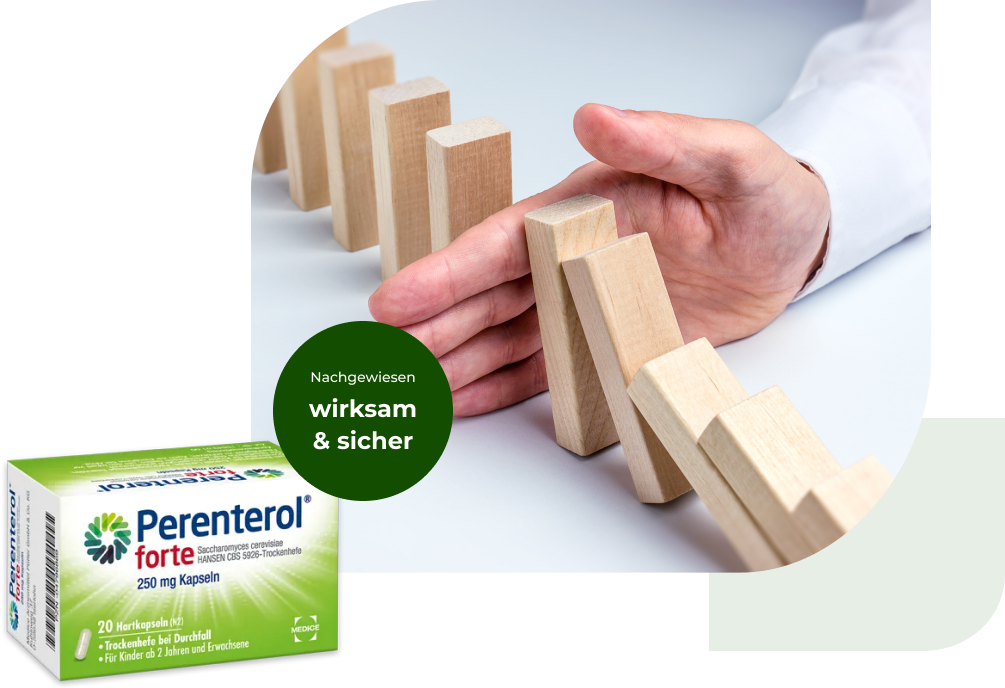 Eine Perenterol forte Verpackung, mit ein paar umfallenden Dominosteinen, die von einer Hand gestoppt werden im Hintergrund
